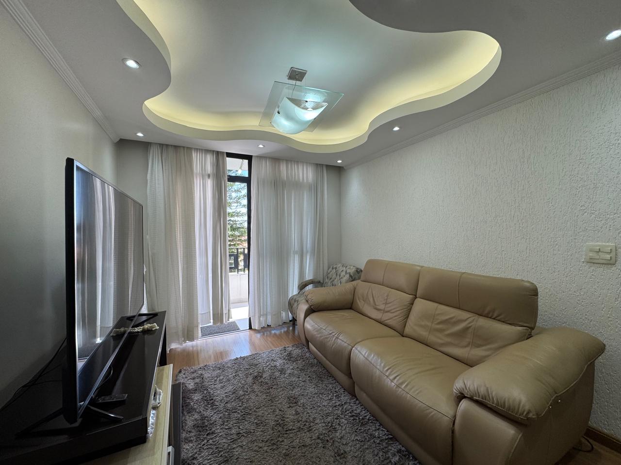 Sala de TV com painel de madeira, sofá de couro e iluminação decorativa no teto de gesso